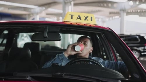Young Man Taxi Driver Drinks Coffee in Car