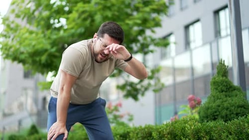 Adult male runner is short of breath after a morning run along a park alley on a city street.