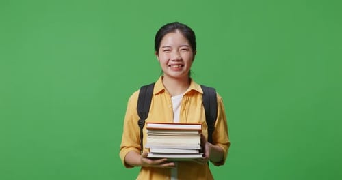 Asian Woman Student With A Backpack Holding Some Books And Smiling In The Green Screen Background