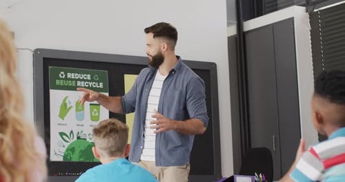 Diverse male teacher and happy schoolchildren at desk in school classroom