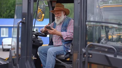 Senior Man Using Smartphone in Tractor