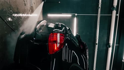 close-up A male car wash employee applies car wash detergent to a black luxury car using spray gun