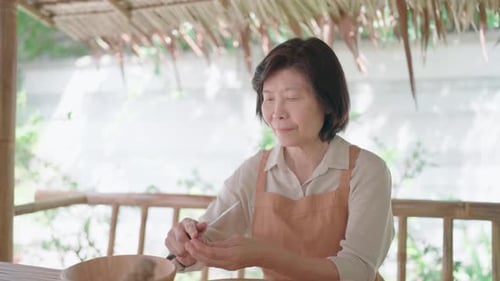 Close-up of Asian senior woman using knife to peel small shallots to prepare traditional Thai food