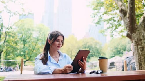 Attractive Stunning Young Caucasian Woman Using Tablet Online Sitting in Picturesque Park Working