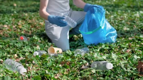 Man collecting plastic garbage in bag in a polluted park. Rubber gloves, recycling sign on T-shirt