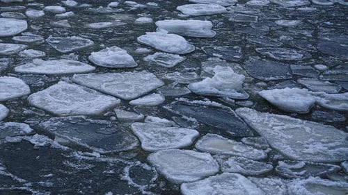 Thin ice fragments rotate near lake edge as winter ice breaks apart