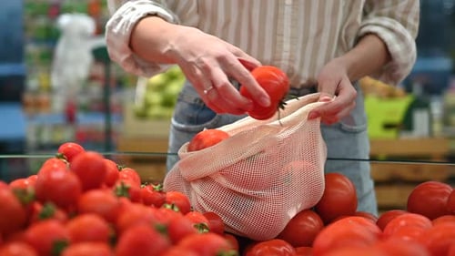 Mujer recogiendo tomates en una bolsa reutilizable en una tienda. Temáticas del Día de la Tierra y la Ecología. Cámara lenta