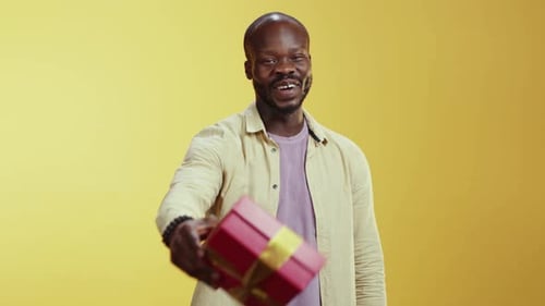 Un homme vêtu d'une chemise blanche et d'un pull violet présente joyeusement des cadeaux