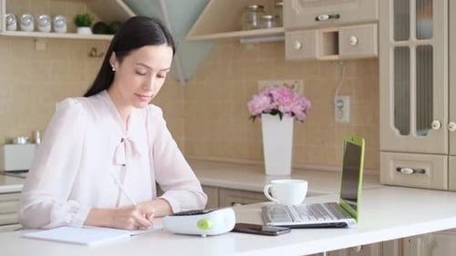 Woman Writes in Notebook at Kitchen Counter