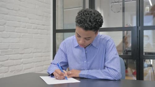 Young African Woman Writing a Letter in Office