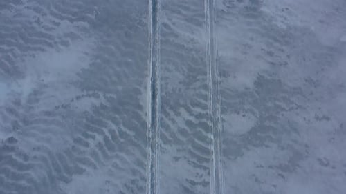 Aerial TOP DOWN flying backwards over snowmobile tracks in the slushy snow on a frozen lake