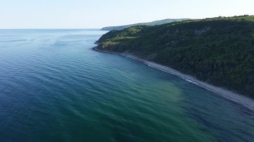 Beach Between a Ledge Covered with Vegetation and a Black Sea Under a Clear Blue Sky