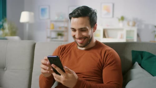 Smiling Man Using Smartphone on Sofa Indoors