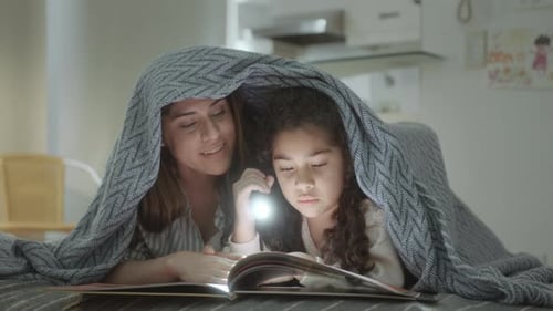 Mother and Daughter Reading Under Blanket with Flashlight