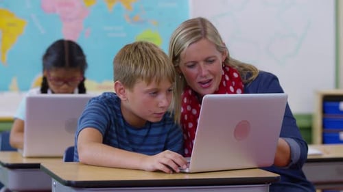Teacher Helping a Student with a Laptop in Class