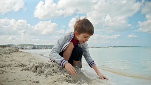 A carefree boy plays on the beach with sand and waves