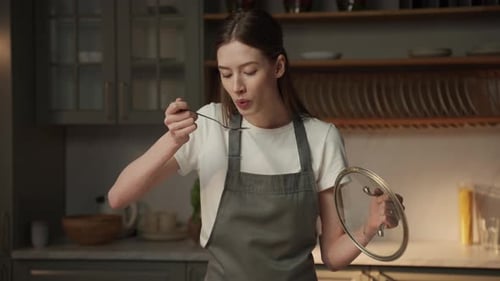 Woman Tastes Food with Spoon in Modern Kitchen