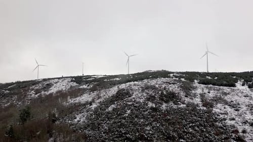 Snowy hill with 3 modern windmills on a cloudy day. Aerial shot