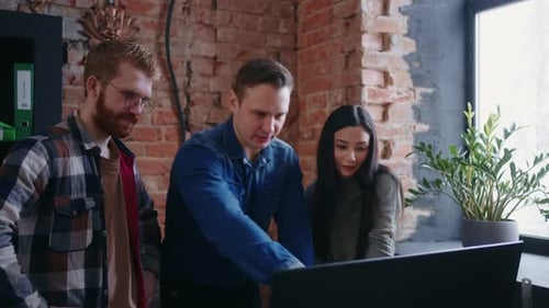 Equipe multiétnica de designers discutindo projeto que examina a tela do computador no escritório