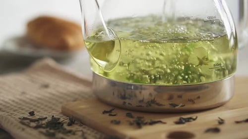 Brew green tea in glass teapot on bamboo board. Pour hot water in kettle with fresh jasmine flower
