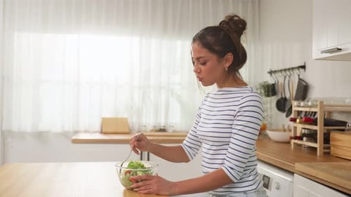 Caucasian young woman eating healthy green salad in kitchen at home.