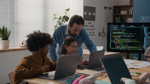 Männlicher Programmierlehrer überprüft Kinder, die im Unterricht an Laptops arbeiten