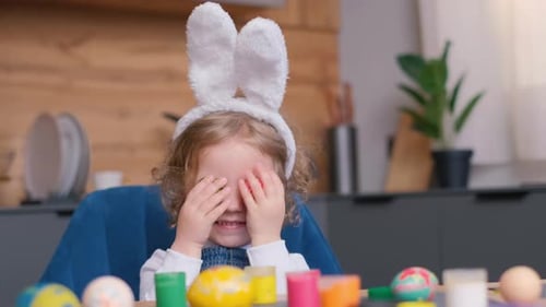 Ein kleines Mädchen mit Hasenohren sitzt in einem Hochstuhl mit Ostereiern