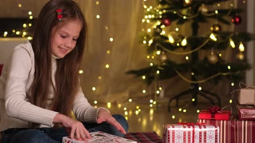 Little Girl Opening Christmas Gift in Decorated Room and Gets Upset