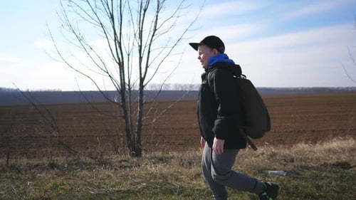 Little Boy in Cap Jogs Near Plowed Field at Early Spring Male Child in Jacket Runs Near Ploughed
