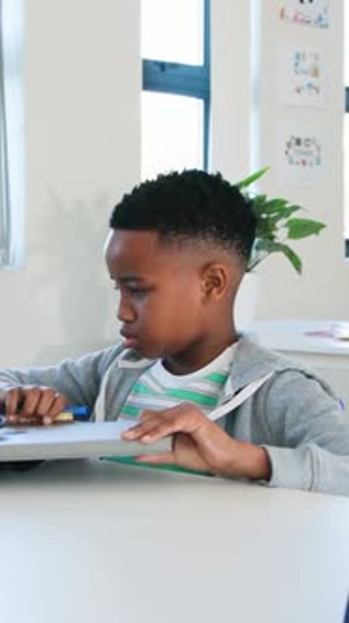 Vertical video: Grabbing backpack, kid in hoodie placing closed laptop and pen at desk to study