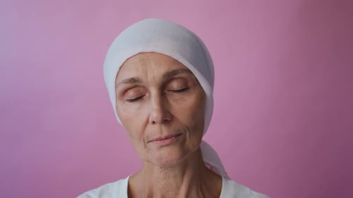 Reife Krebspatientin mit Kopftuch blickt auf rosa Farbe in die Kamera
