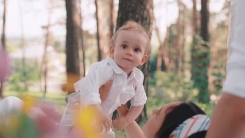 Positive family lying on blanket in park. Attractive woman hugging child