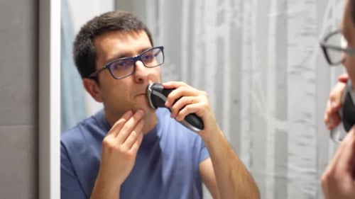 Man Shaving Face with Electric Razor in Bathroom