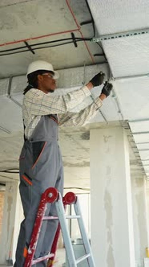 Electrician Installing Cables on a Ladder in Building Under Construction