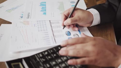 Close Up of a Businessman Hands with Pen Working at Office Desk and Analyzing Graphs and Charts and