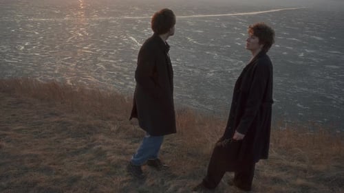 Couple Sharing Cigarette and Talking on Frozen Lake Shore at Sunset