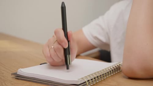 Female hand rhythmically tapping pen end on spiral notebook page with audio