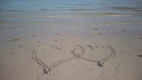 Statische Aufnahme von zwei ineinandergreifenden Herzen an einem Strand mit Wasser, wenn sie am Strand plätschern.