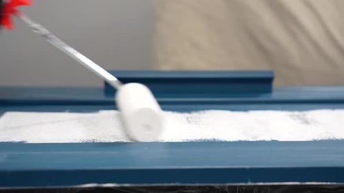 White Paint Roller Applies Paint To Blue Surface