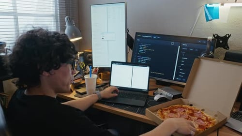 Man Coding Software on Laptop and Eating Pizza in Home Office