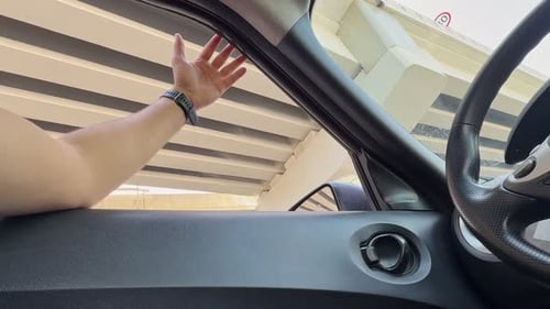 Handgeste des Fahrers aus dem Autofenster unter der Autobahnüberführung während der Fahrt im Stadtverkehr
