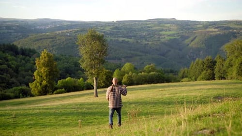 Lumberjack walking with an axe on his shoulder in a beautiful countryside scenery, with green mounta