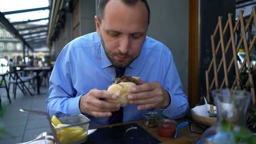 Hungry Businessman Eating Burger And French Fries In Cafe