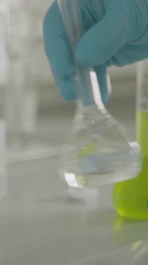 Nahaufnahme eines Wissenschaftlers, der im Labor mit einer Flasche mit grüner Flüssigkeit umgeht