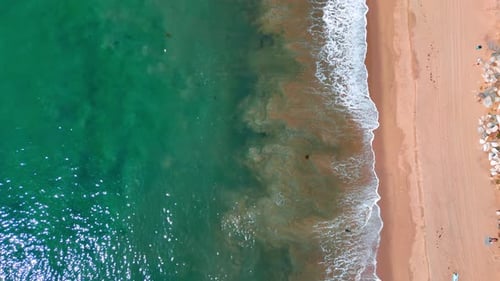 Flight over the place where sea meets the shore. Waves slowly splash on the sandy beach