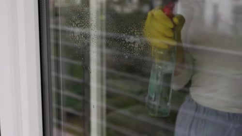 Woman, housework and housekeeping concept - woman in gloves cleaning window with rag and cleanser sp