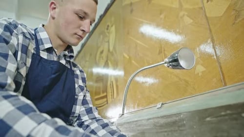 A Young Man Manually Lathing a Piece of Timber with a Chisel in a Workshop