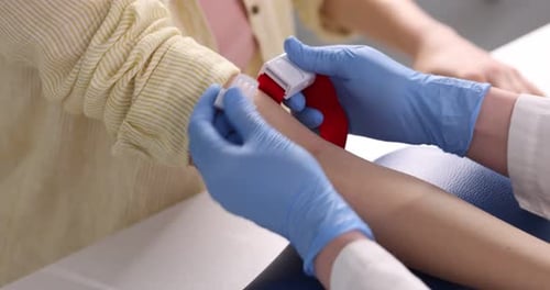 Nurse putting medical tourniquet on patient's arm at white table in clinic, closeup