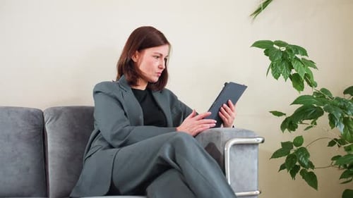 Businesswoman in Suit Using Digital Tablet on Couch in Modern Office