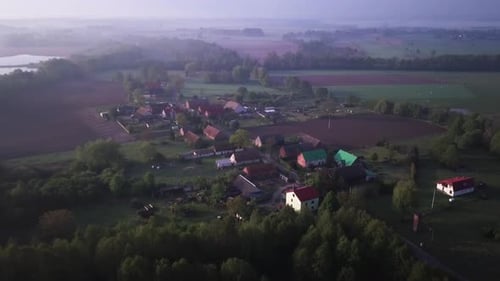 4k footage of a village near lake surrounded by forest from birds eye perspective. Sunrise and fog o
